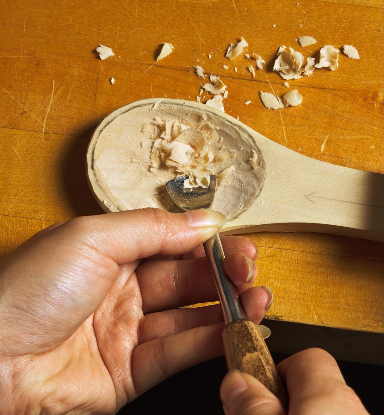 A carving chisel being used to carve out the bowl of a wooden spoon.