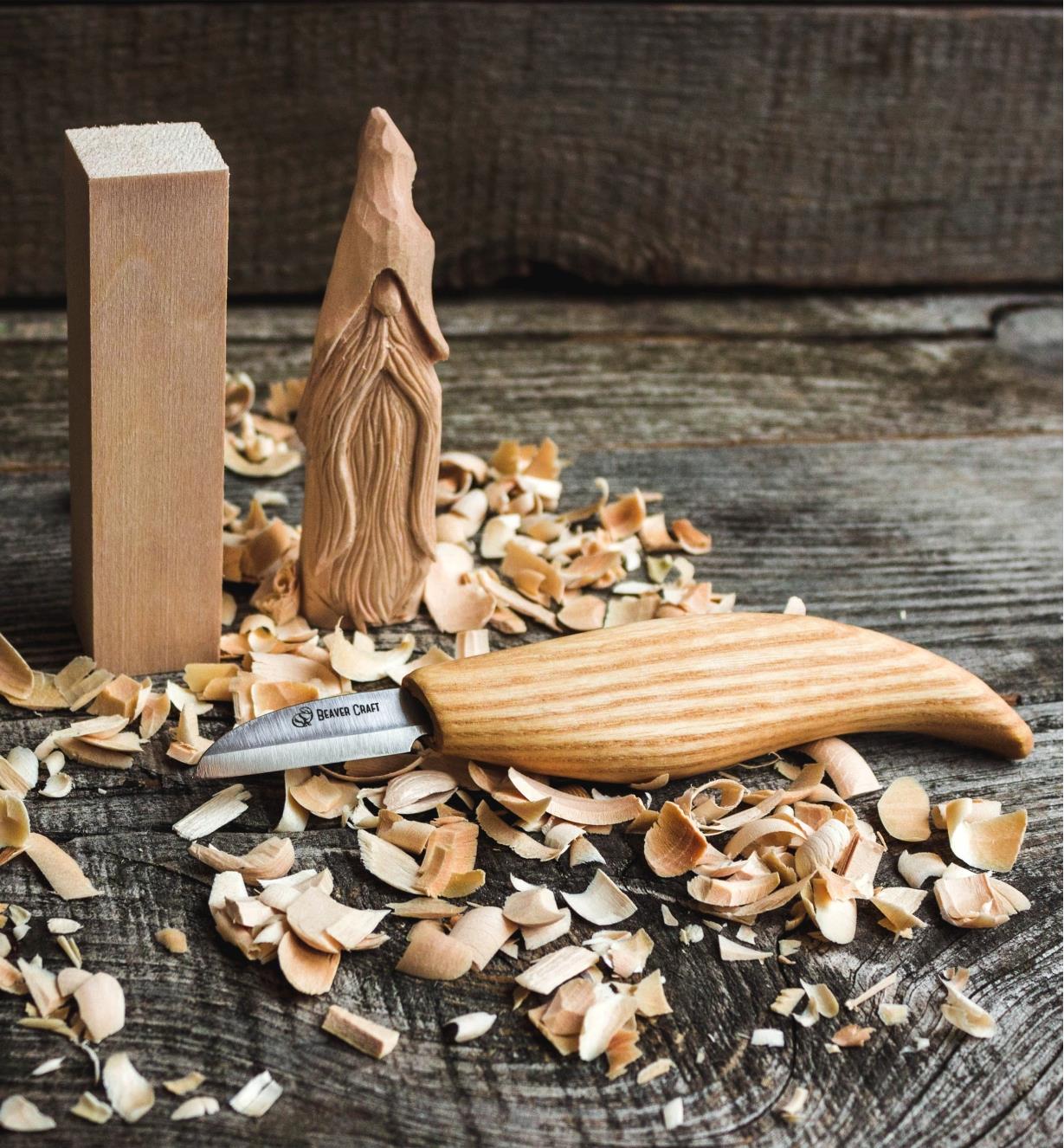 A wood blank, a finished wizard carving and a carving knife displayed on wood shavings
