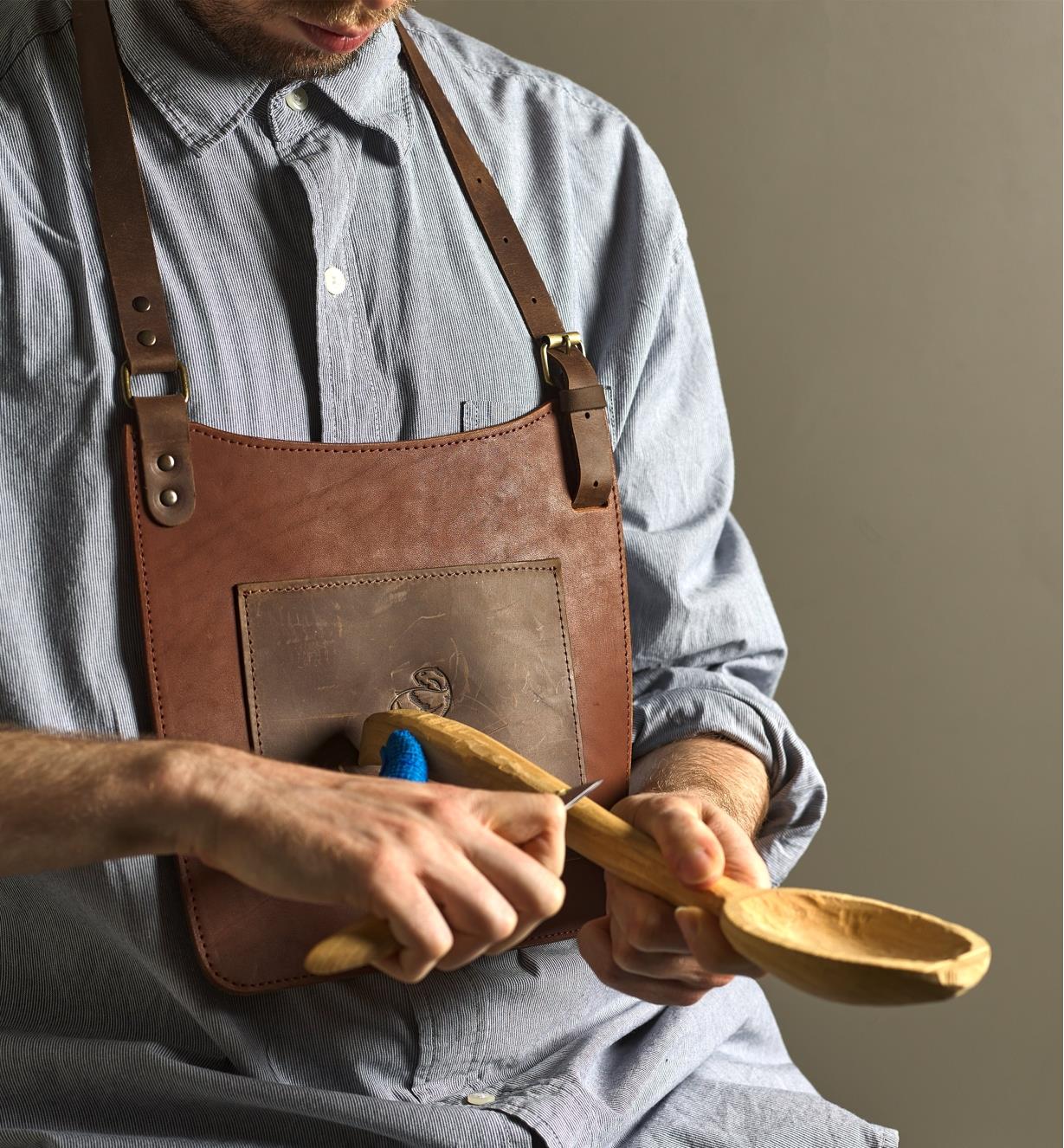 A carver wears a BeaverCraft chest apron while carving a wooden spoon