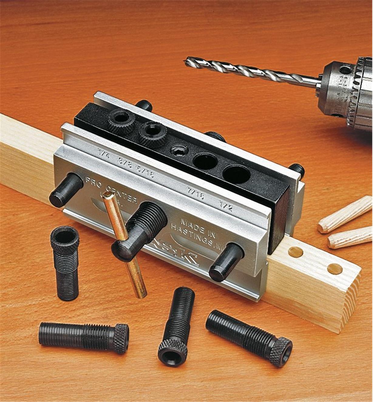 The Self-Centering Dowelling Jig secured to a board, with a power drill and dowel pins next to it