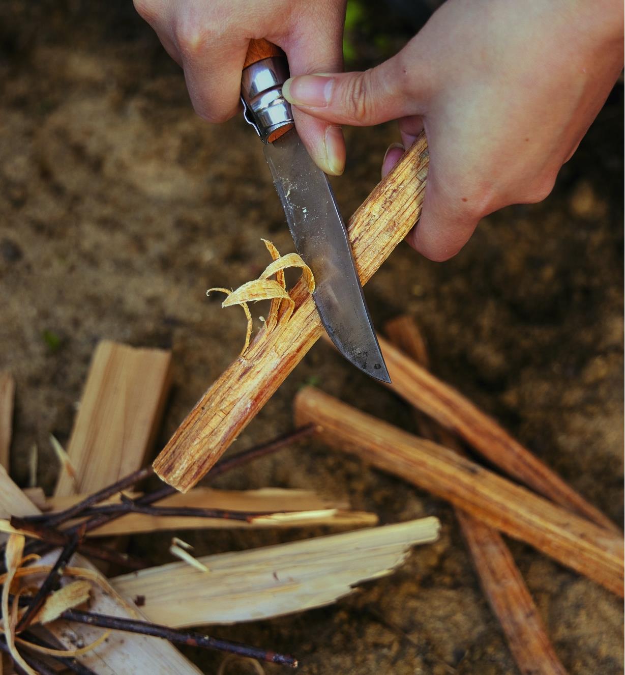 Scraping a Fatwood stick with a knife before lighting a campfire