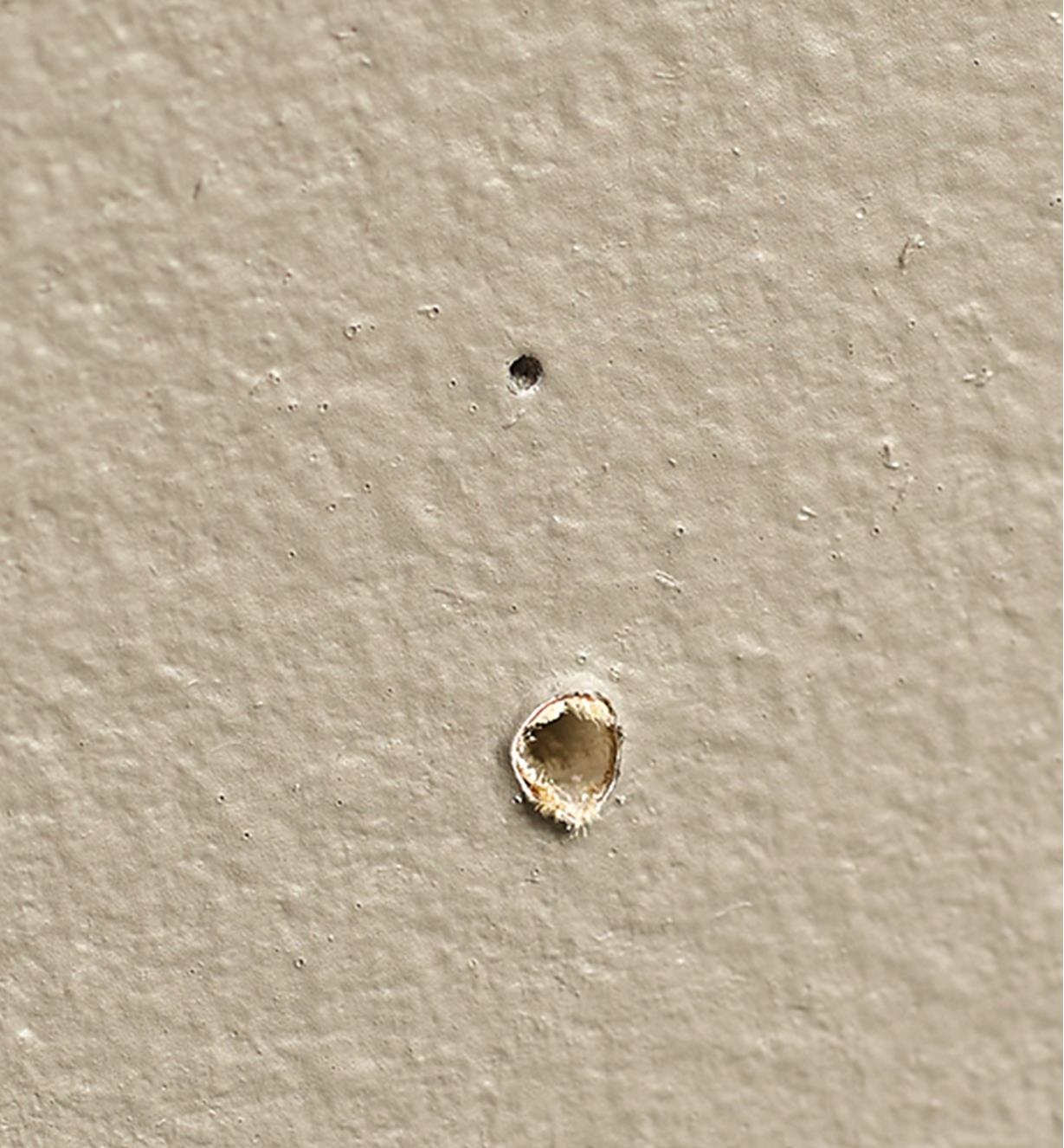 One small hole and one larger hole on a piece of drywall