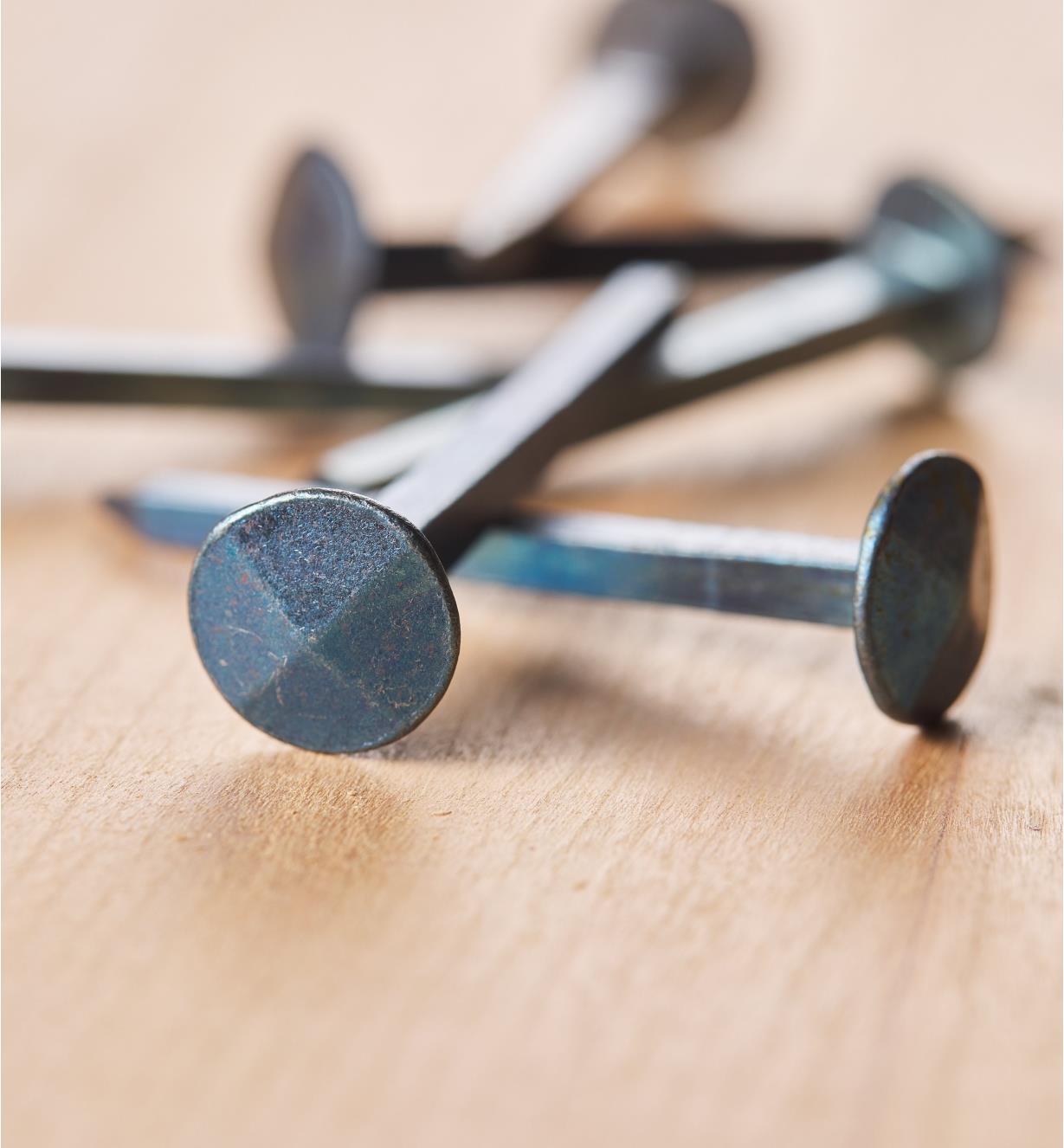 Several Blued Steel Forged Nails from Clouterie Rivierre lying on a board.