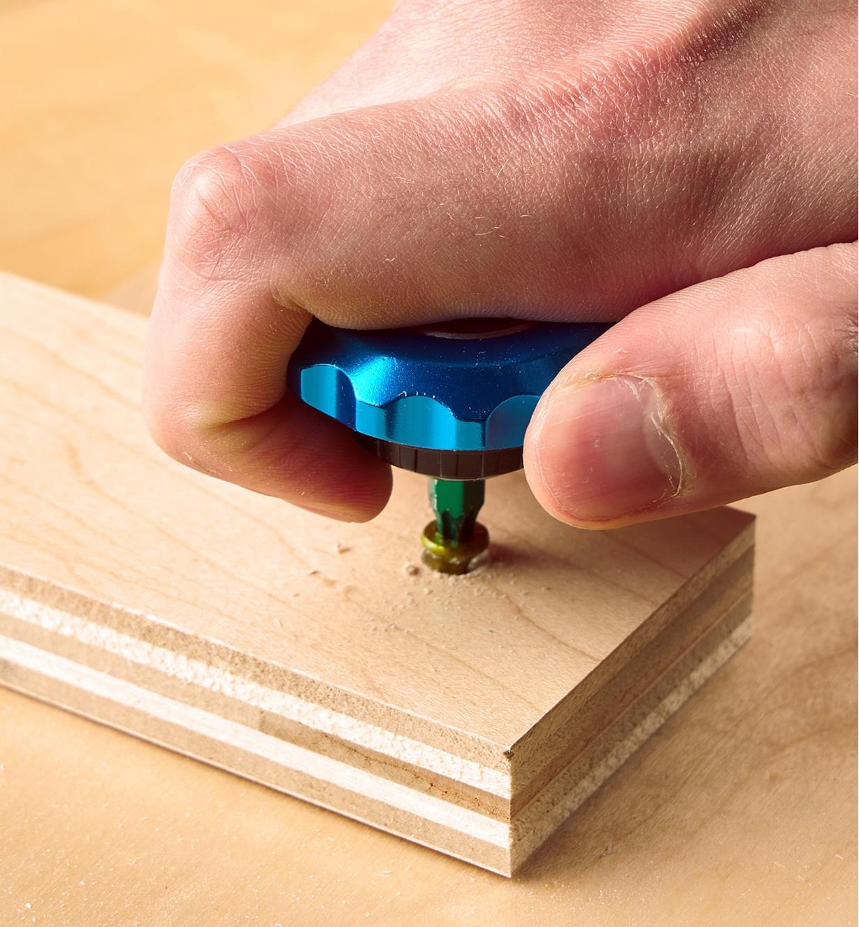 A palm driver being used to drive a screw into a board