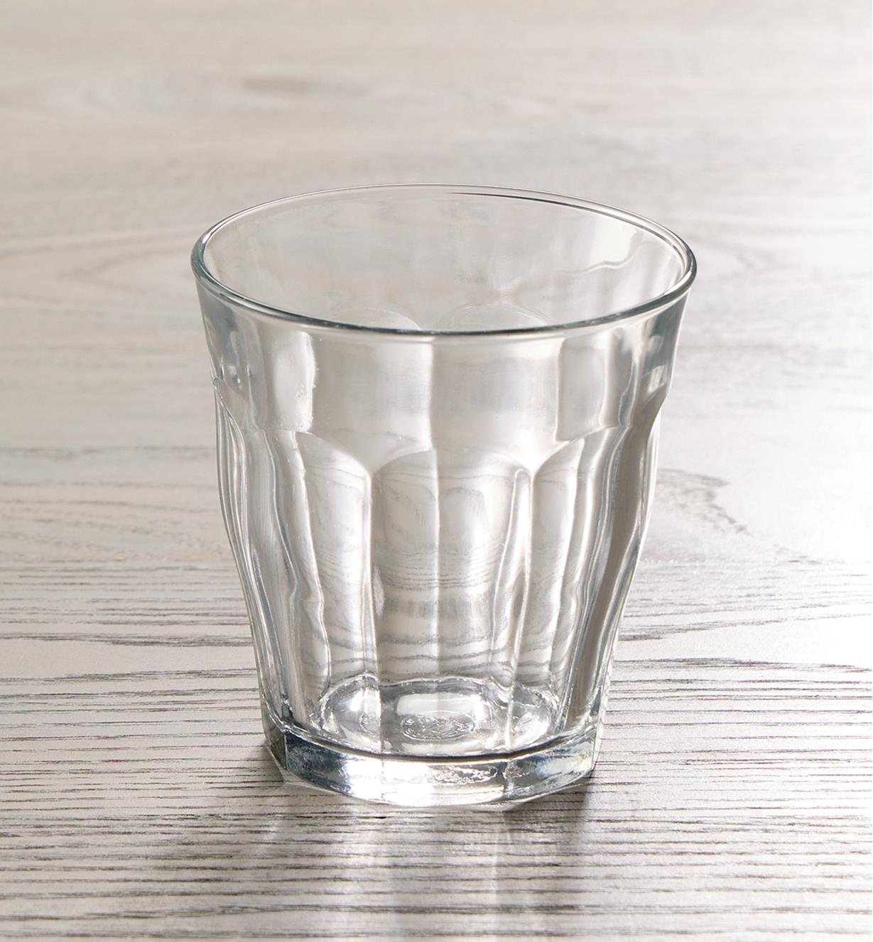 An empty 310ml Duralex Picardie glass placed on a wooden tabletop backlit to show the fluted design
