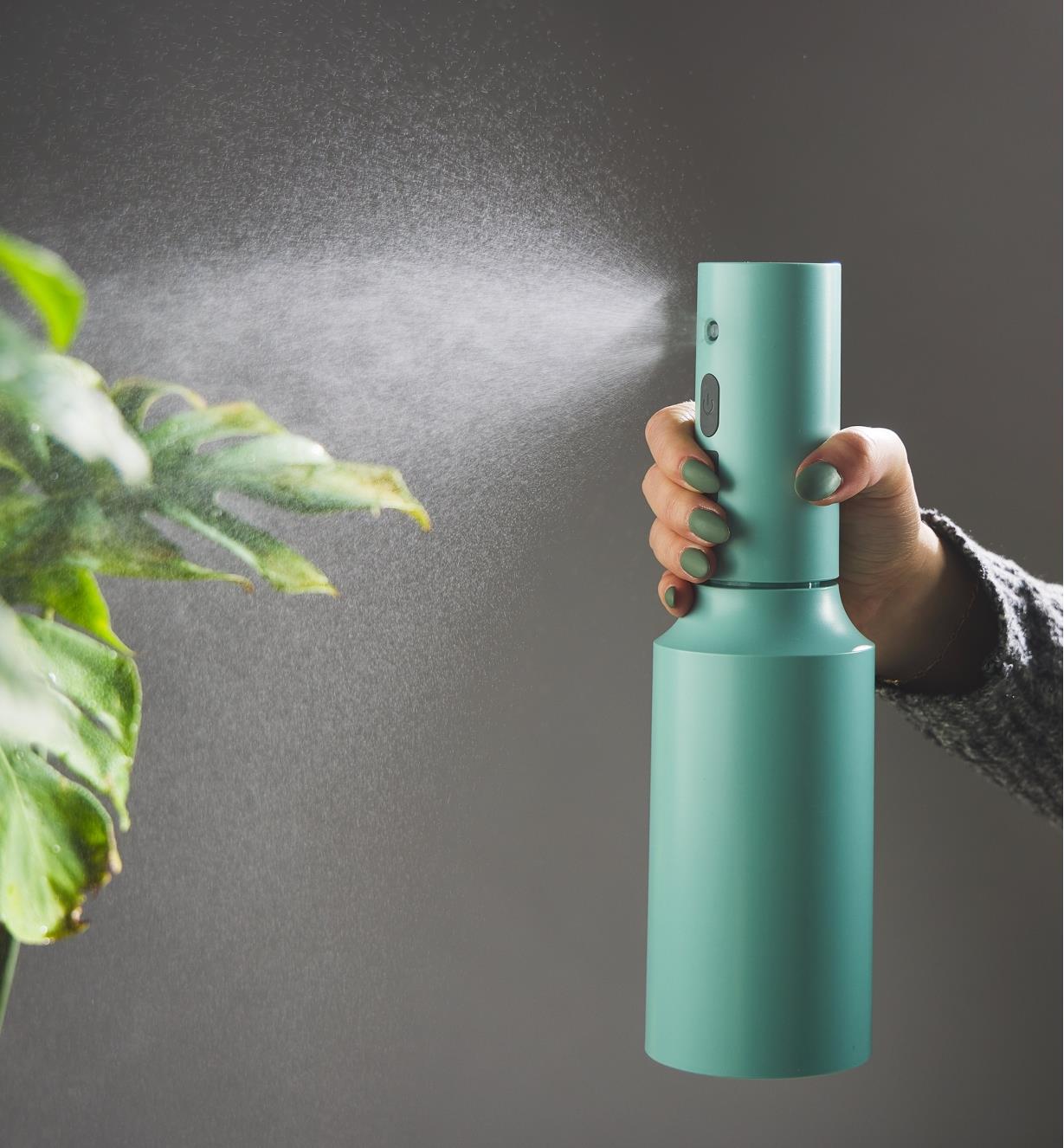 Using a rechargeable plant mister to spray a mist onto the leaves of a plant