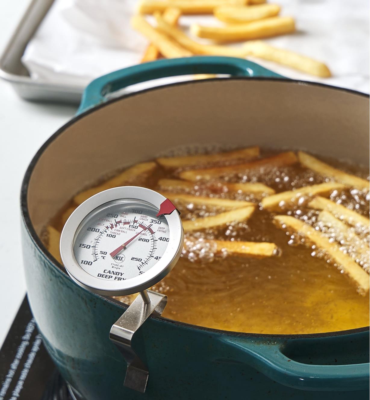 A pot of boiling oil and French fries with a thermometer clipped to the edge