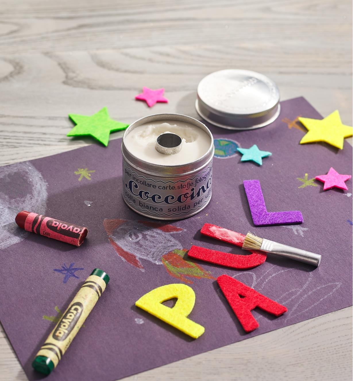 An open tin of paste glue on a piece of purple paper with partially glued cut-out letters