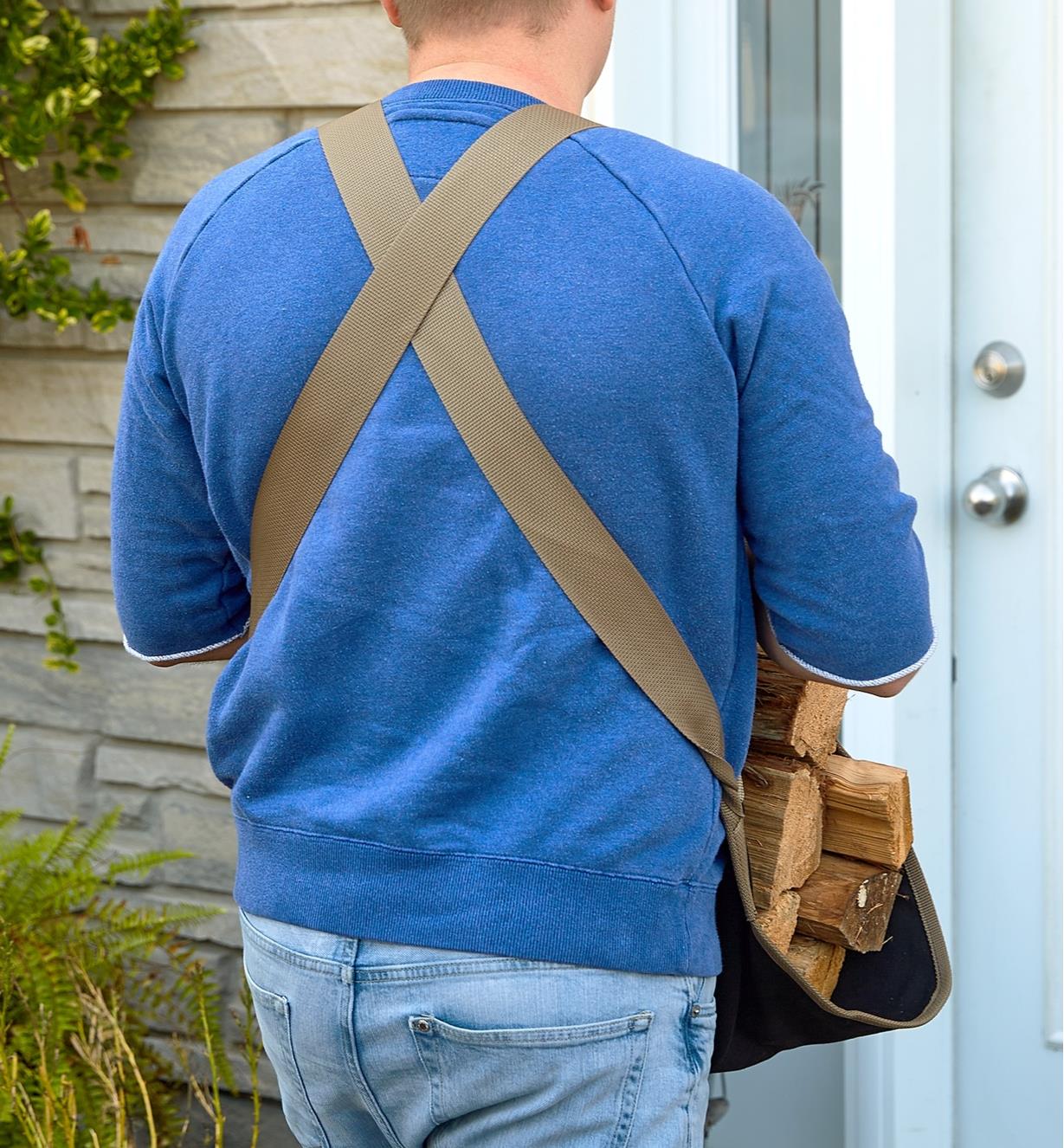 Back view of a man carrying firewood showing the crossed straps of the apron tote