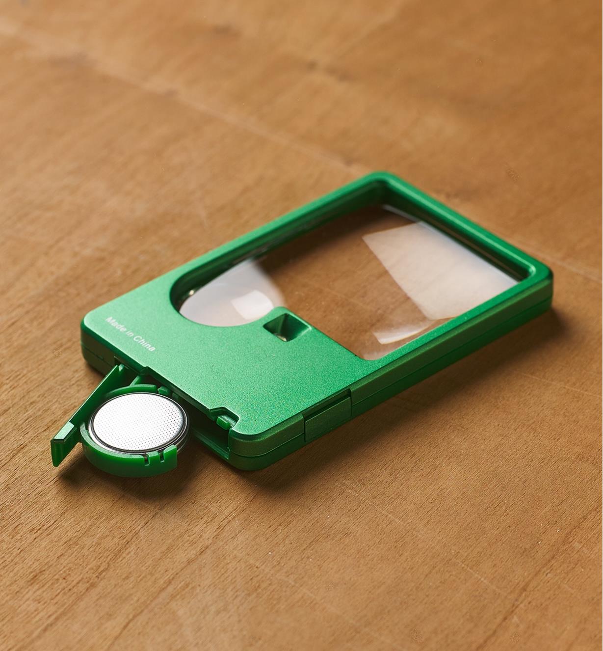 An LED pocket magnifier placed on a tabletop with the battery compartment opened