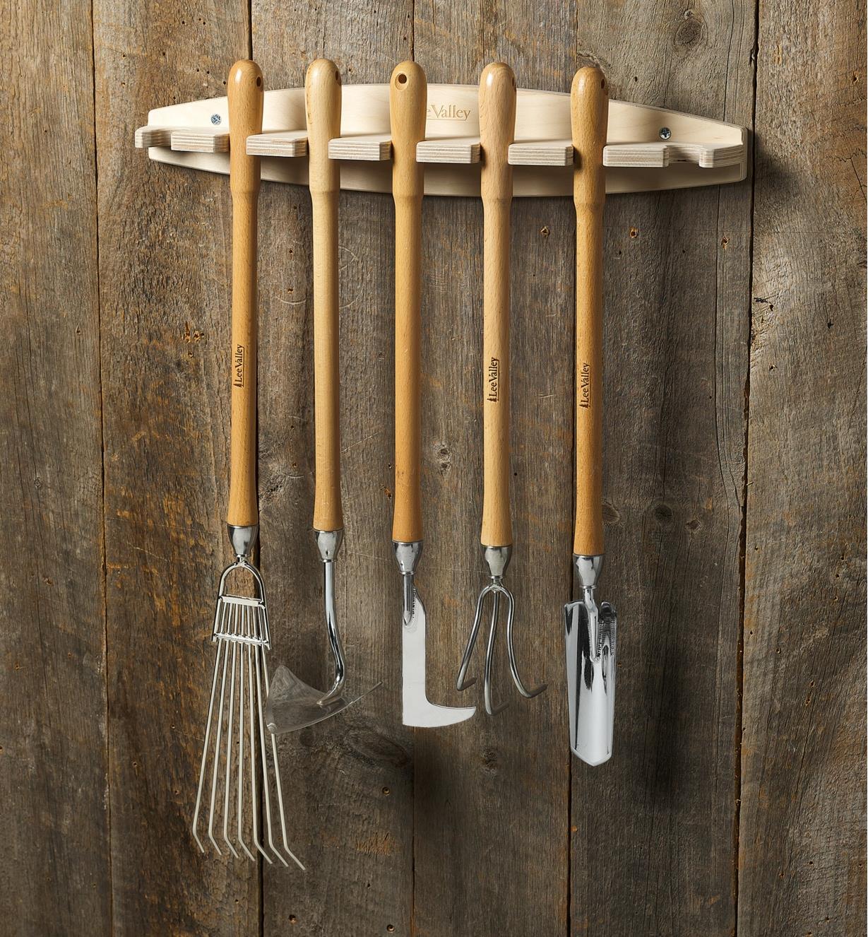 Five mid-length garden tools hanging on a rack mounted on a barnboard shed wall