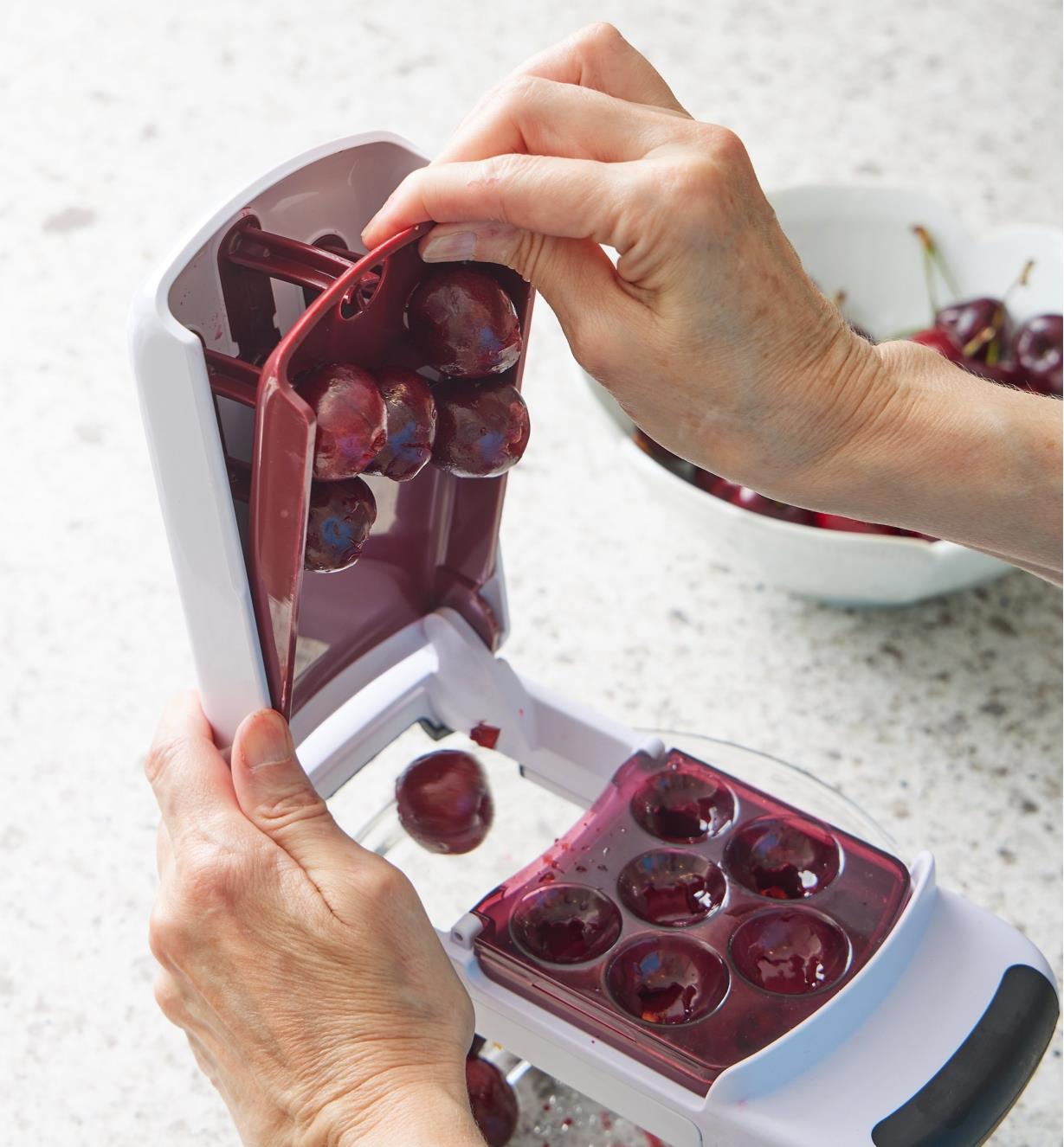 Lifting the top of the multi-cherry pitter to release the cherries into the bowl below