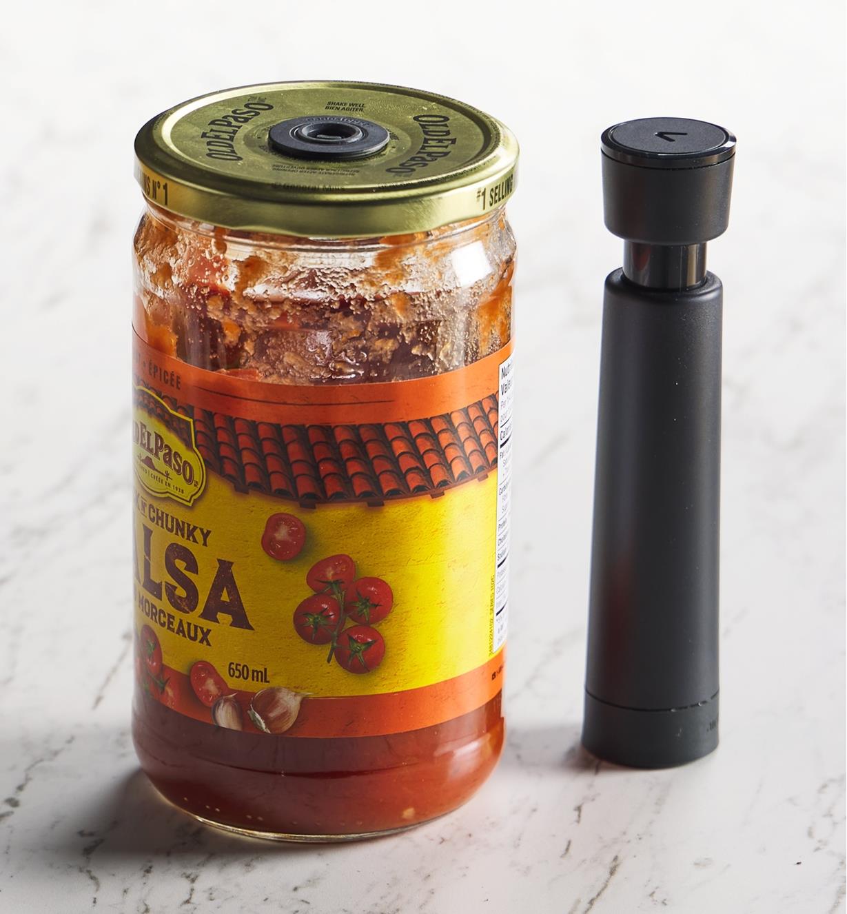 An Airtender hand pump beside a jar of salsa with an Airtender stopper set in the lid