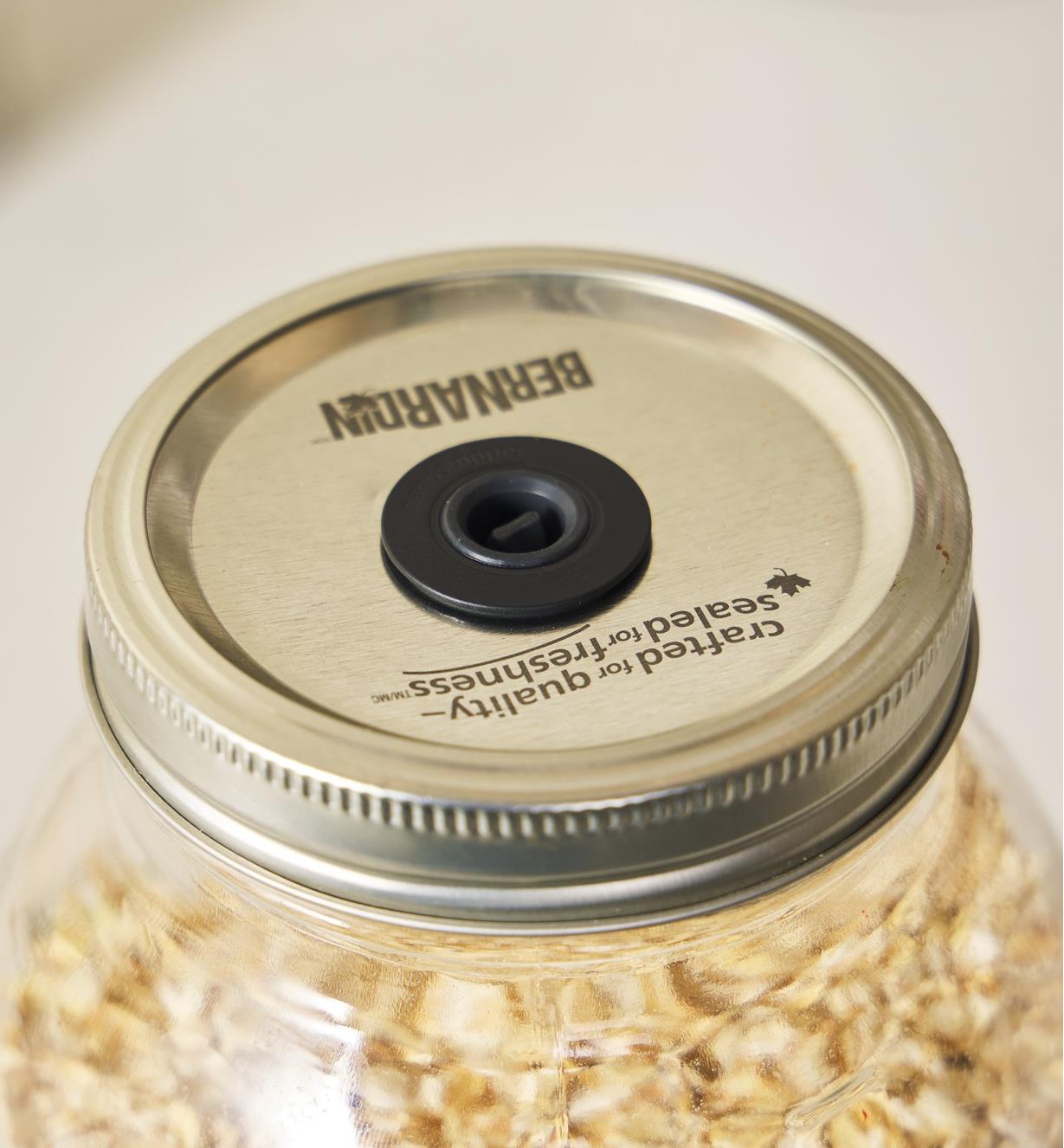 A close-up view of an Airtender stopper valve inserted into a hole cut in the lid of a Mason jar