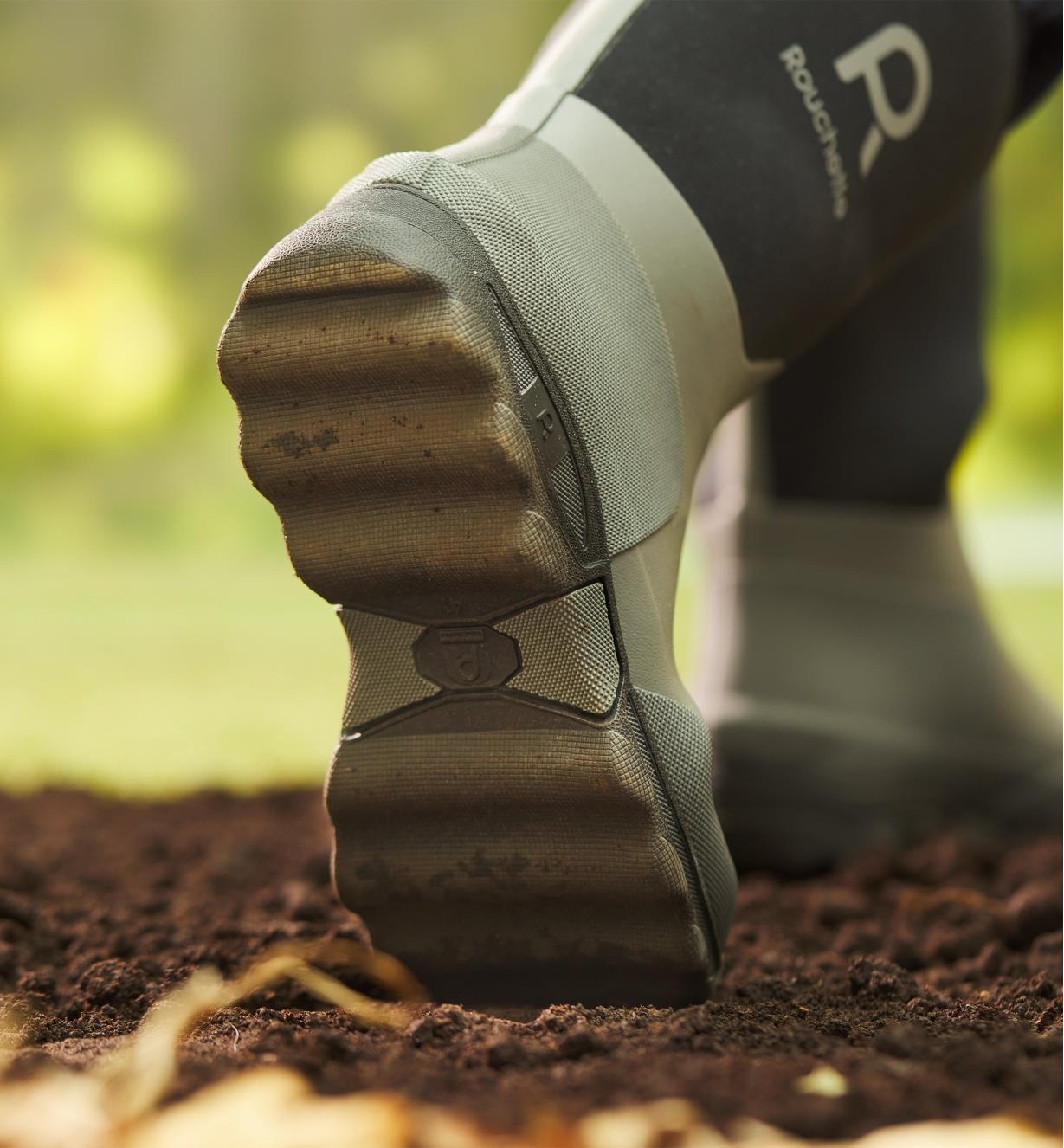 The bottom of a garden boot showing treads on the sole as the person wearing them walks through dirt