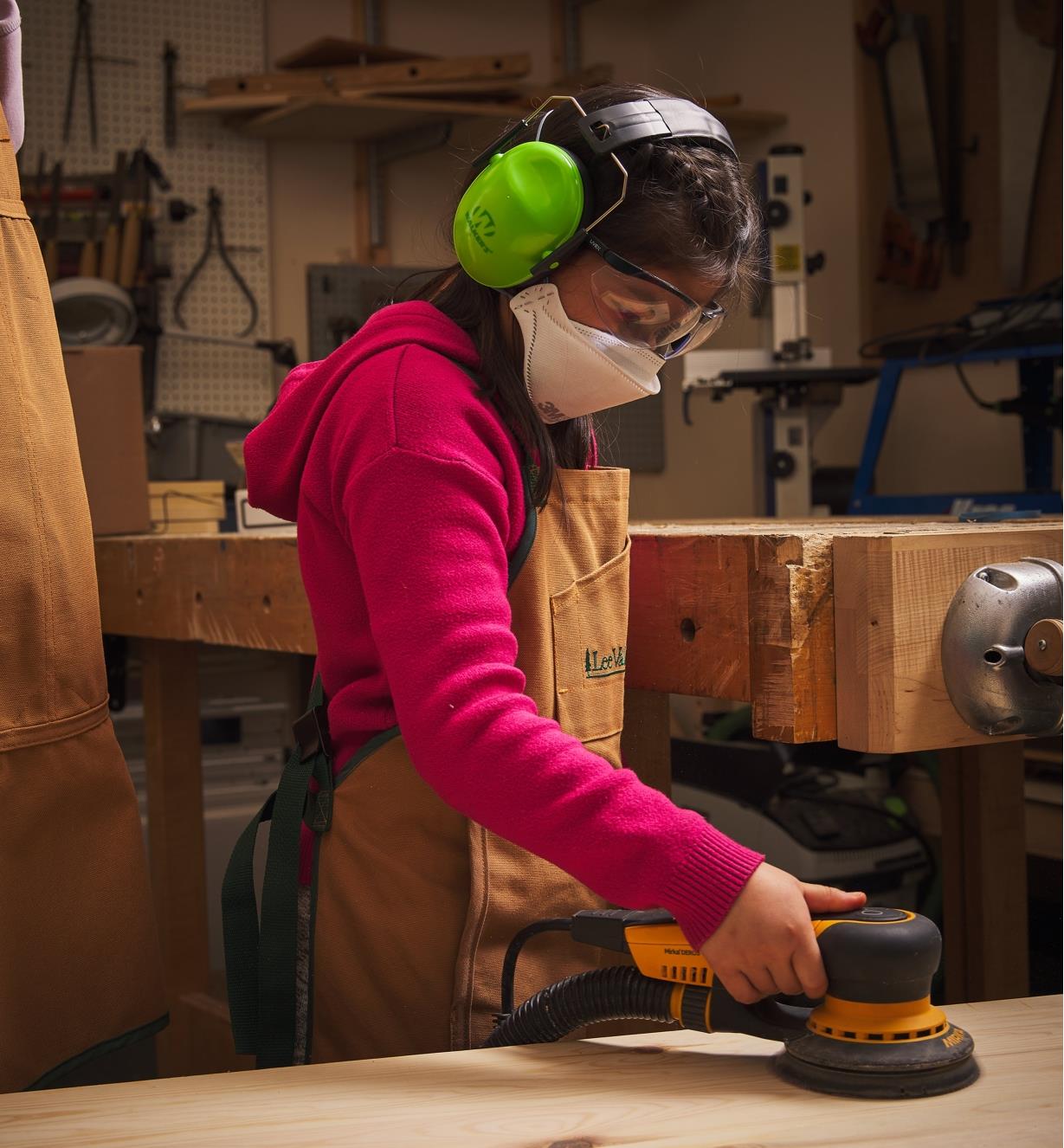 A child sanding wood while wearing hearing protectors, safety glasses and a dust mask