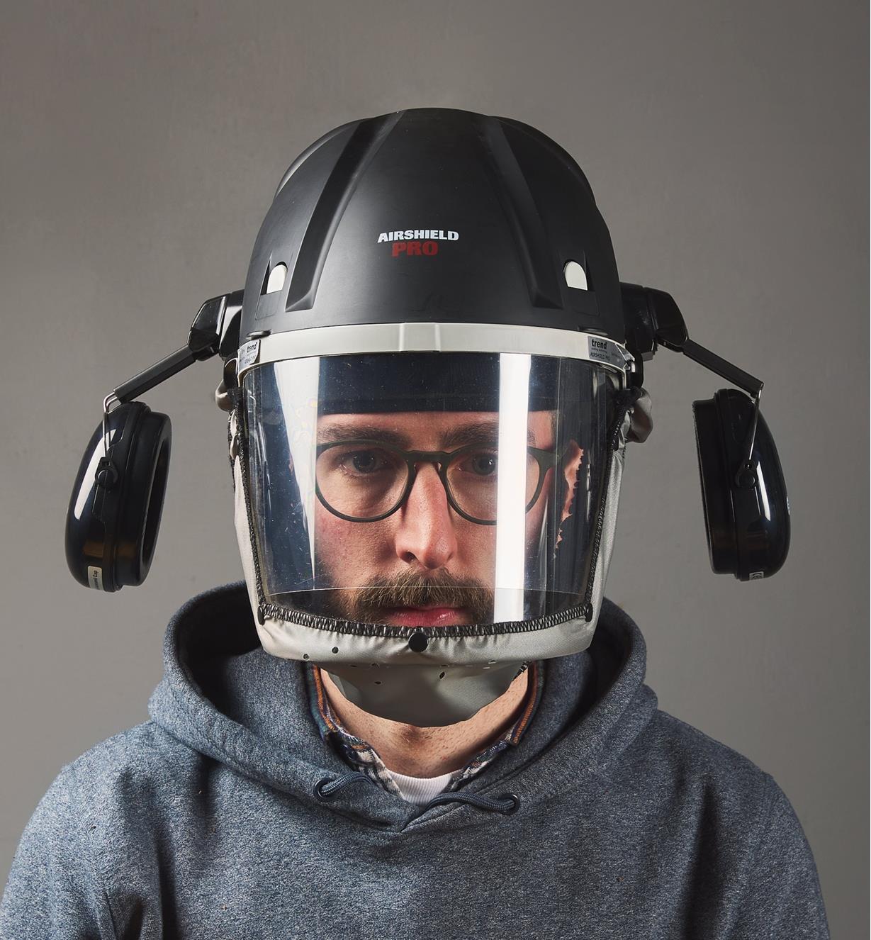 A man wears a Trend Airshield Pro full-face shield with the attached Ear Defenders swung to the sides away from the ears