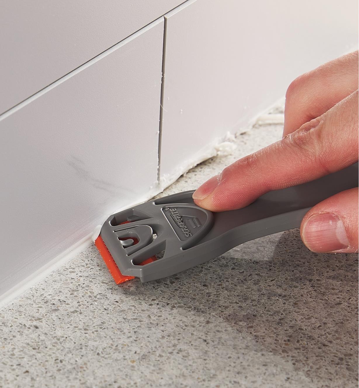 Scraping grout using a razor blade in a holder
