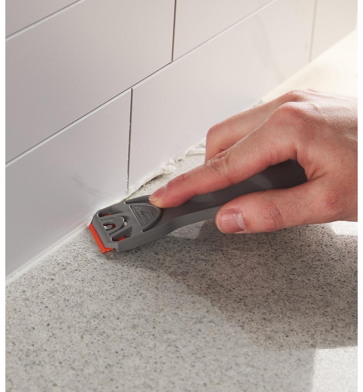 Using a plastic razor blade to remove excess caulking from a countertop