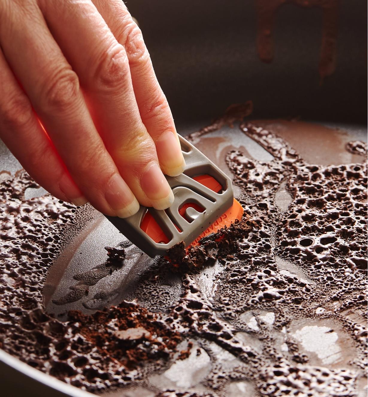 Scraping baked-on food off a pan using a razor blade in a holder