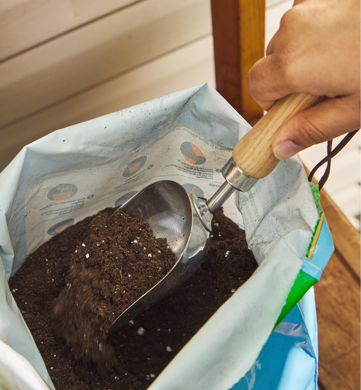 Using a stainless-steel scoop to dig into a bag of soil