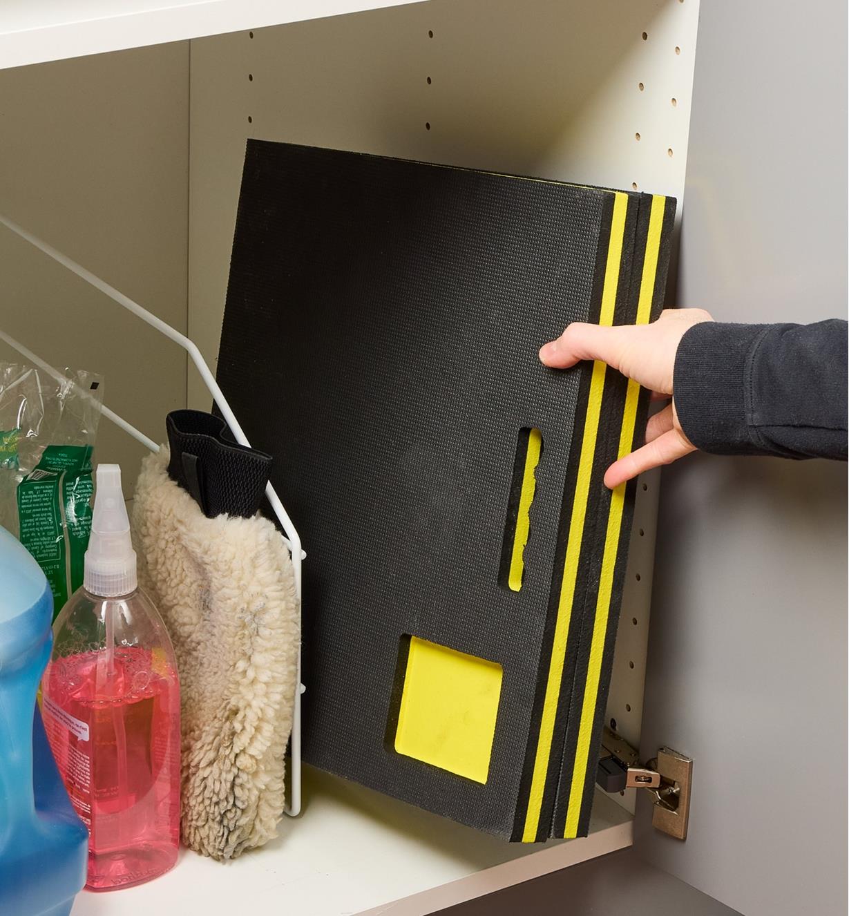 Reaching for a foam kneeler that is folded in half and stored in a cupboard with cleaning supplies