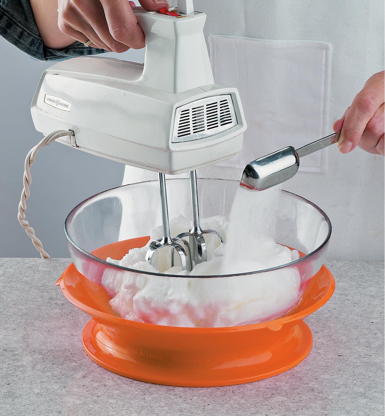 A cook whipping meringue in a glass bowl set on a Staybowlizer