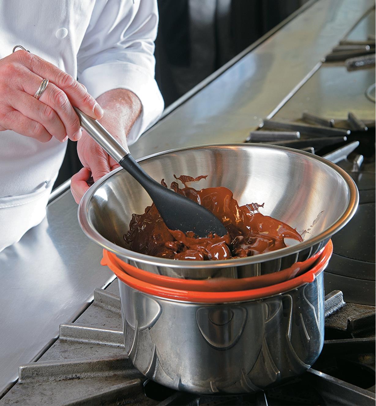A chef melting chocolate in a steel bowl set on a Staybowlizer over a pot of boliling water