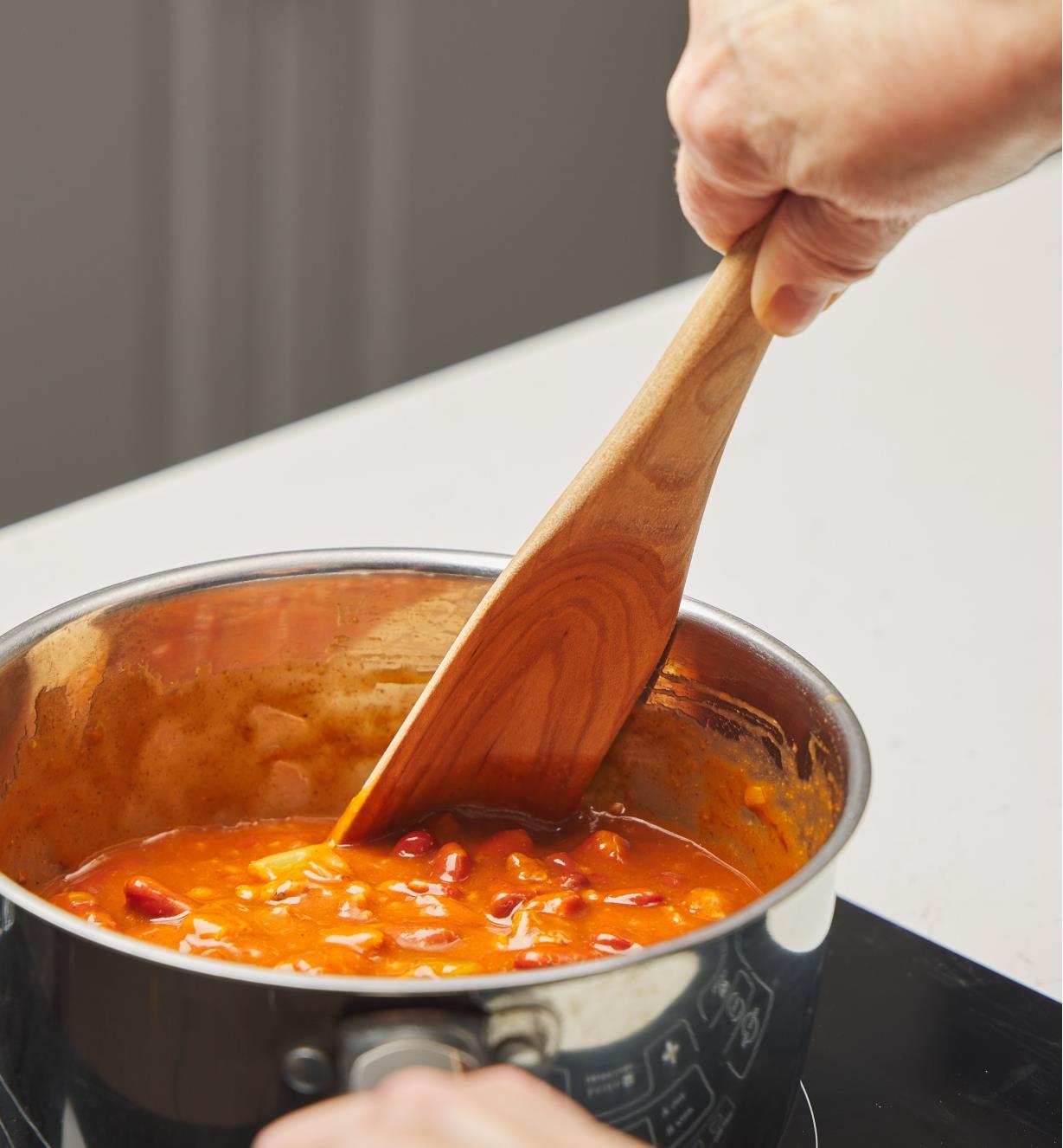 Personne brassant une sauce tomate dans une casserole avec une cuillère-spatule en érable