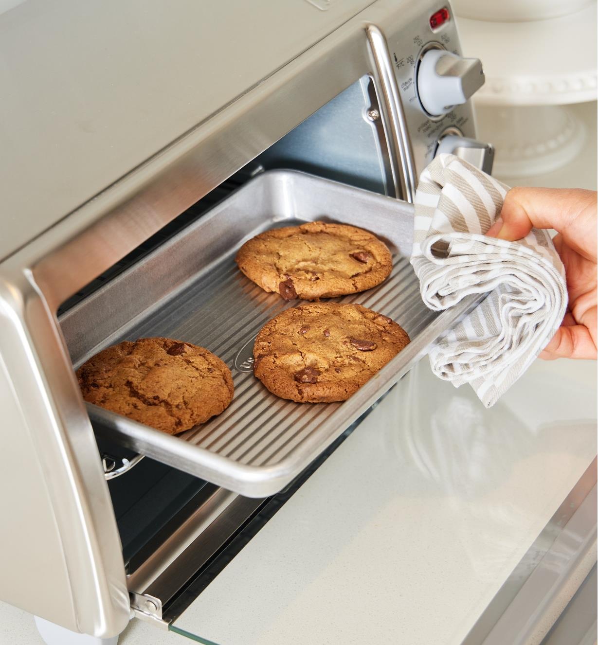 A small batch of cookies baked on an eighth-sheet baking pan being removed from a toaster oven