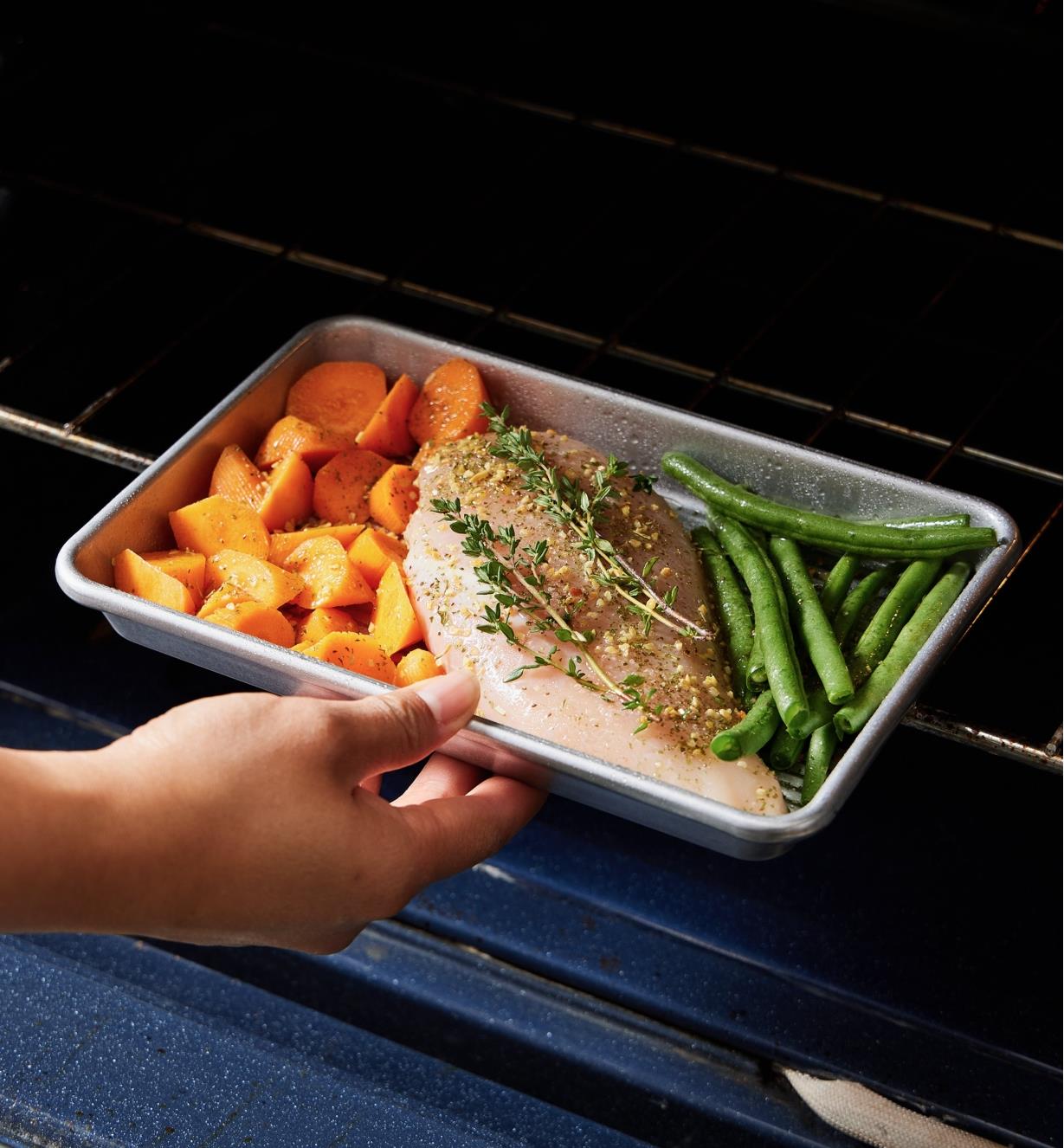 Carrots, asparagus and chicken being placed in an oven on an eighth-sheet baking pan