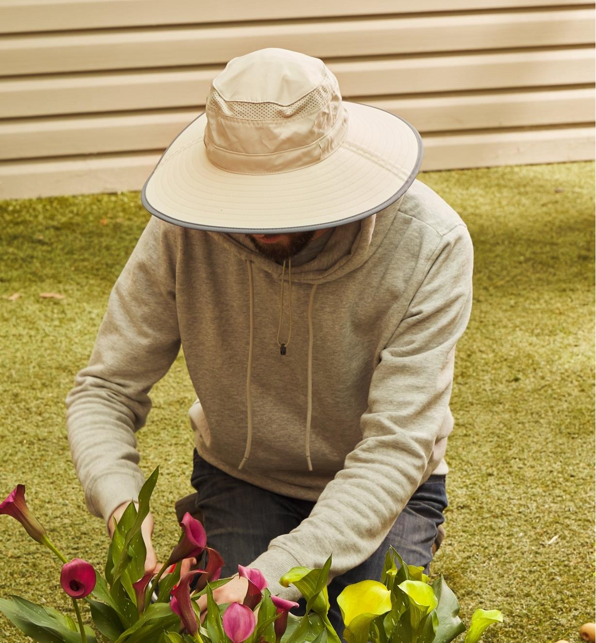 Personne à genoux portant un chapeau à large bord et récoltant des fleurs