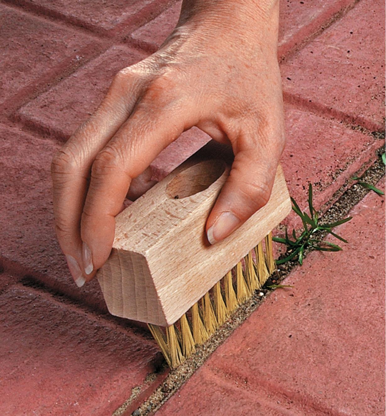 Using a weed brush to clean the cracks between patio stones