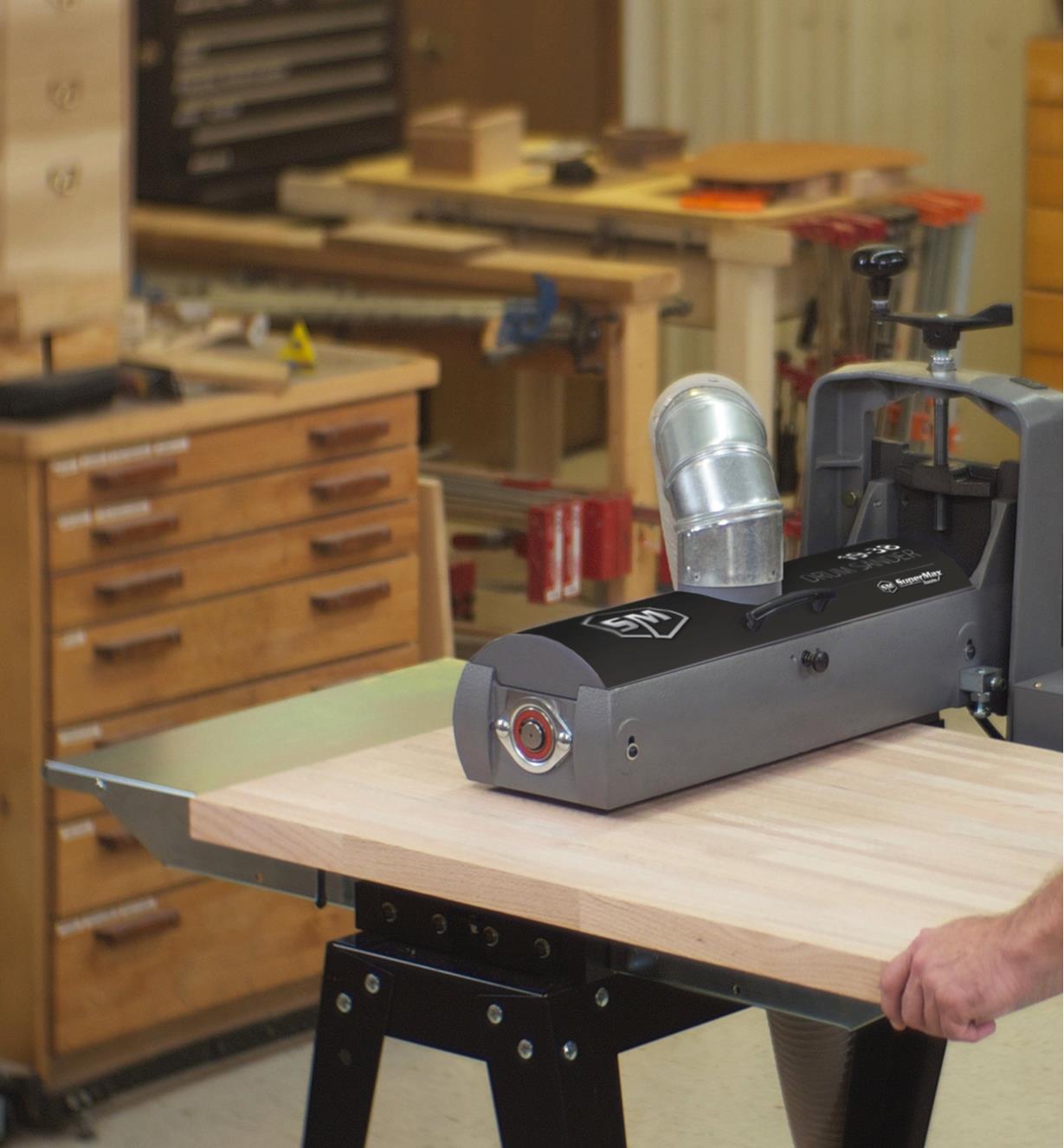 A wide board being fed through a 19-38 drum sander with an infeed/outfeed table