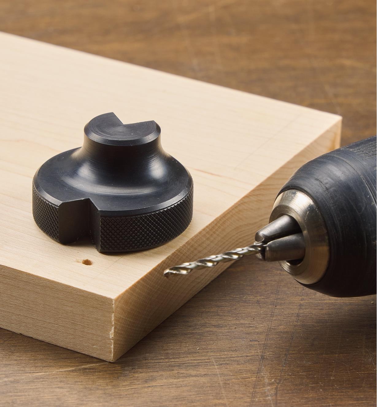A board with a hole drilled in it, with a pocket drilling guide on top and a drill beside it