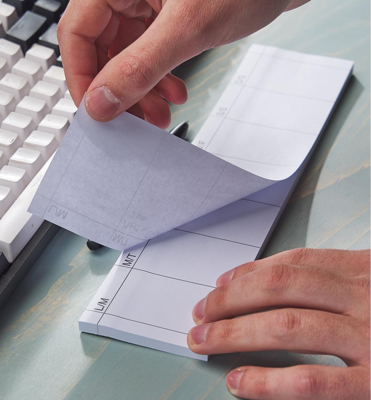 A person tears a page off a weekly tear-off planner pad