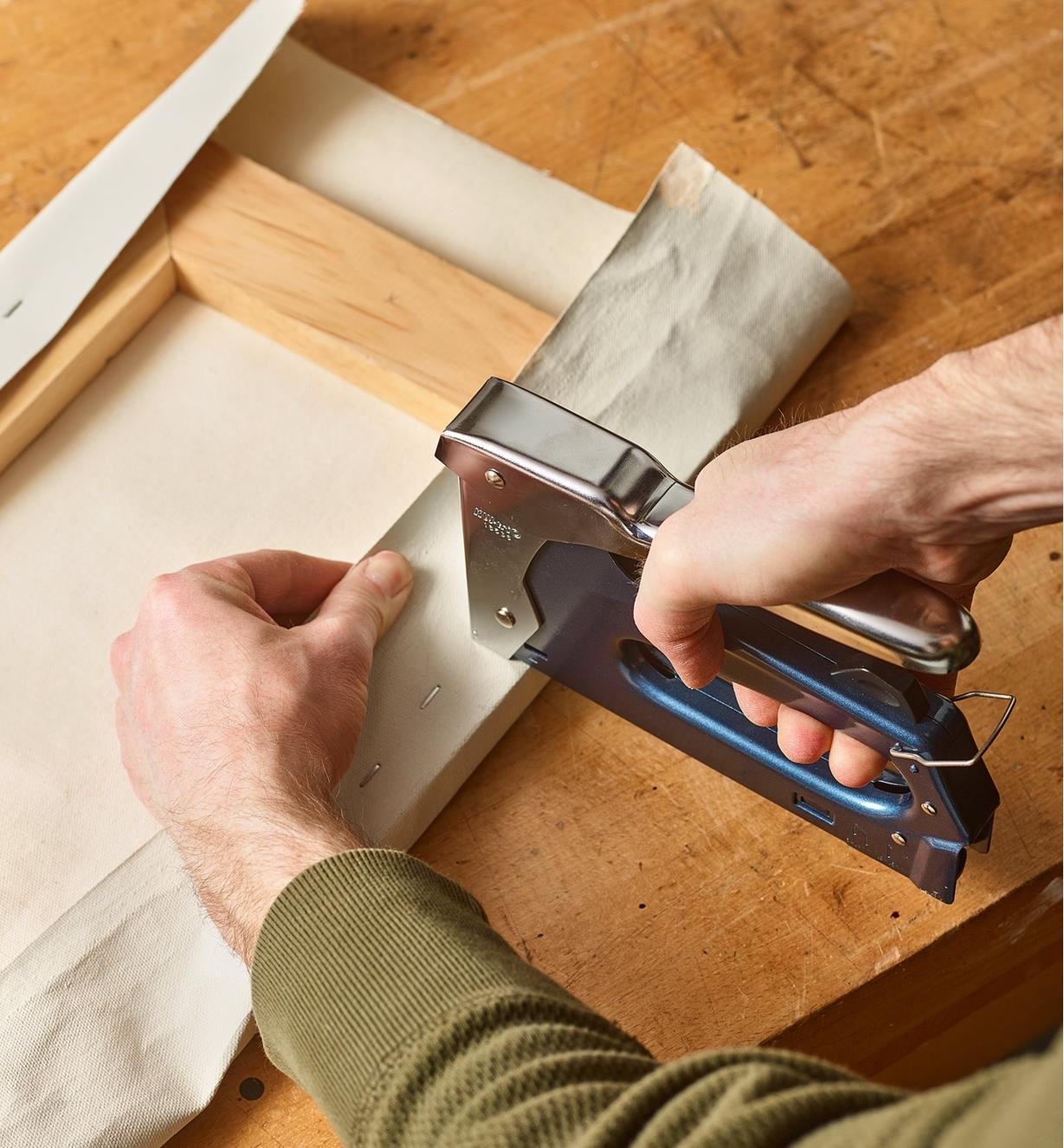 A staple gun being used to staple paper to a wooden frame