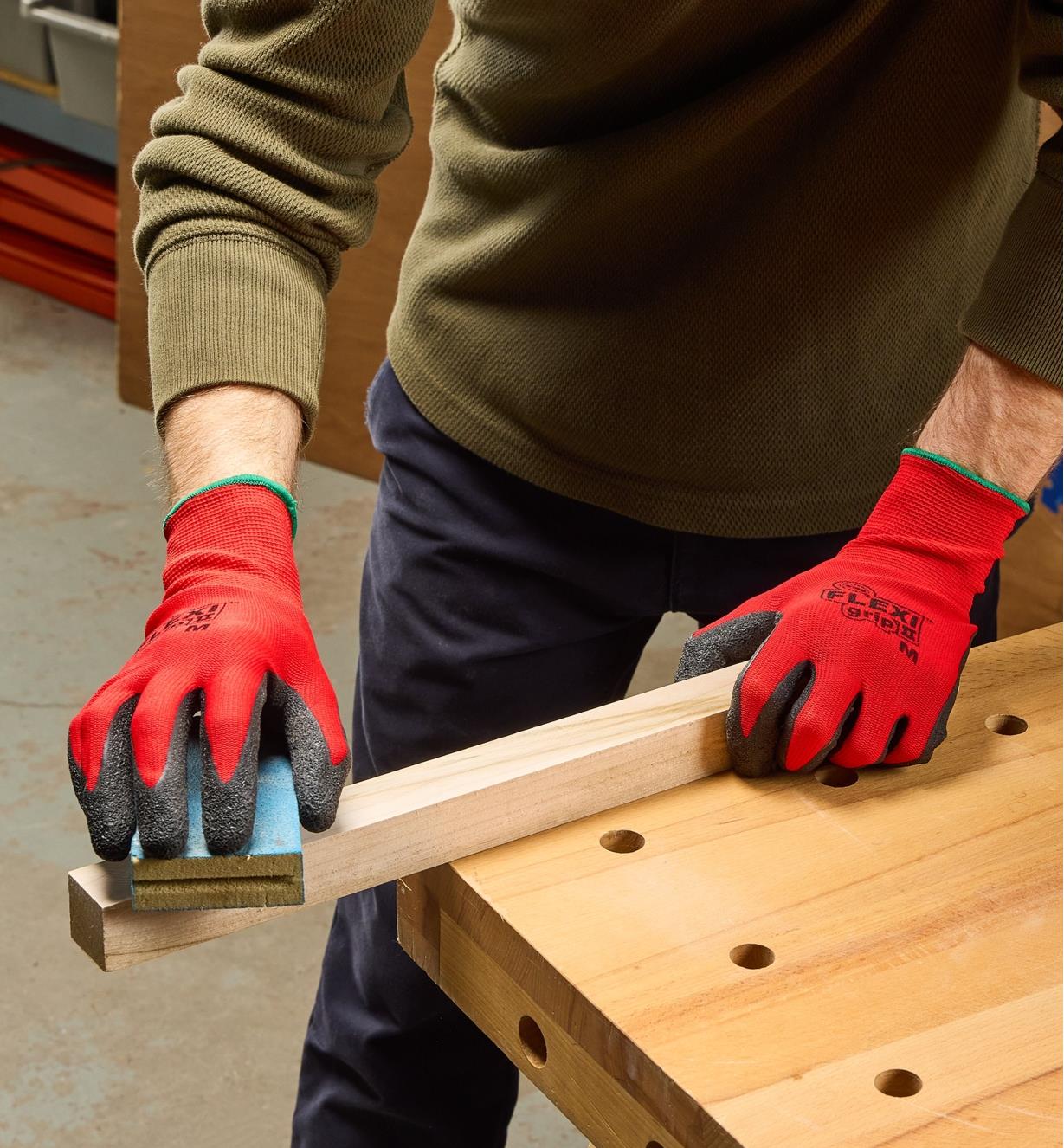 A man wears Flex Grip gloves while sanding a piece of wooden stock