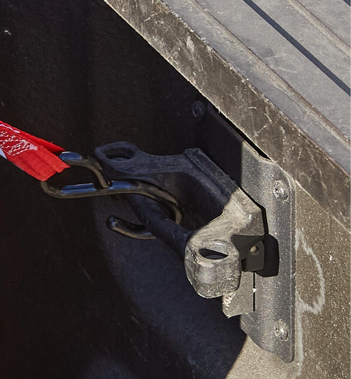 The hook on the end of a Quickloader ratchet strap attached to an anchor point on a pickup truck bed