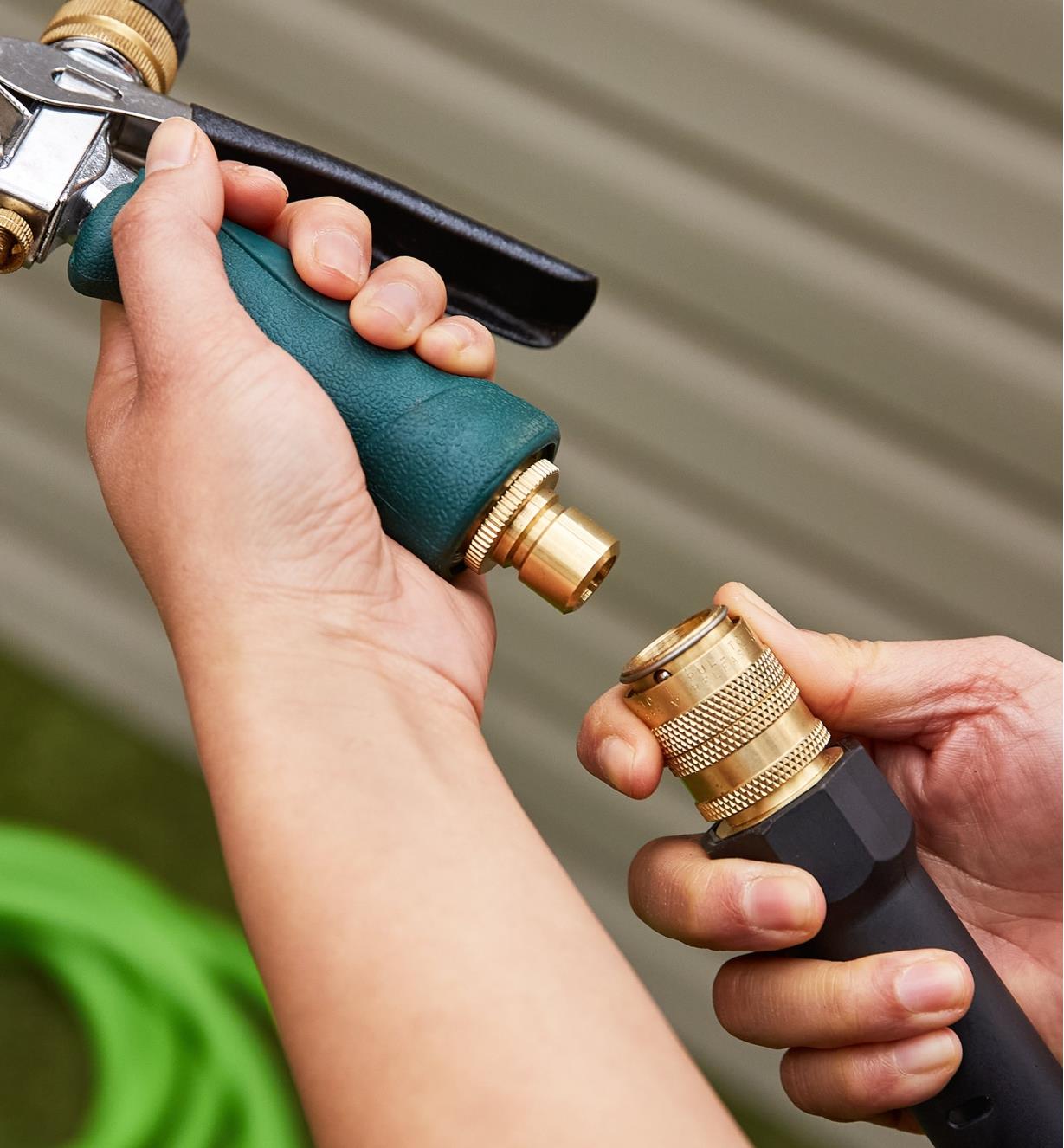A nozzle with a male quick connect is held in one hand with the other hand holding a hose with a female quick connect attached
