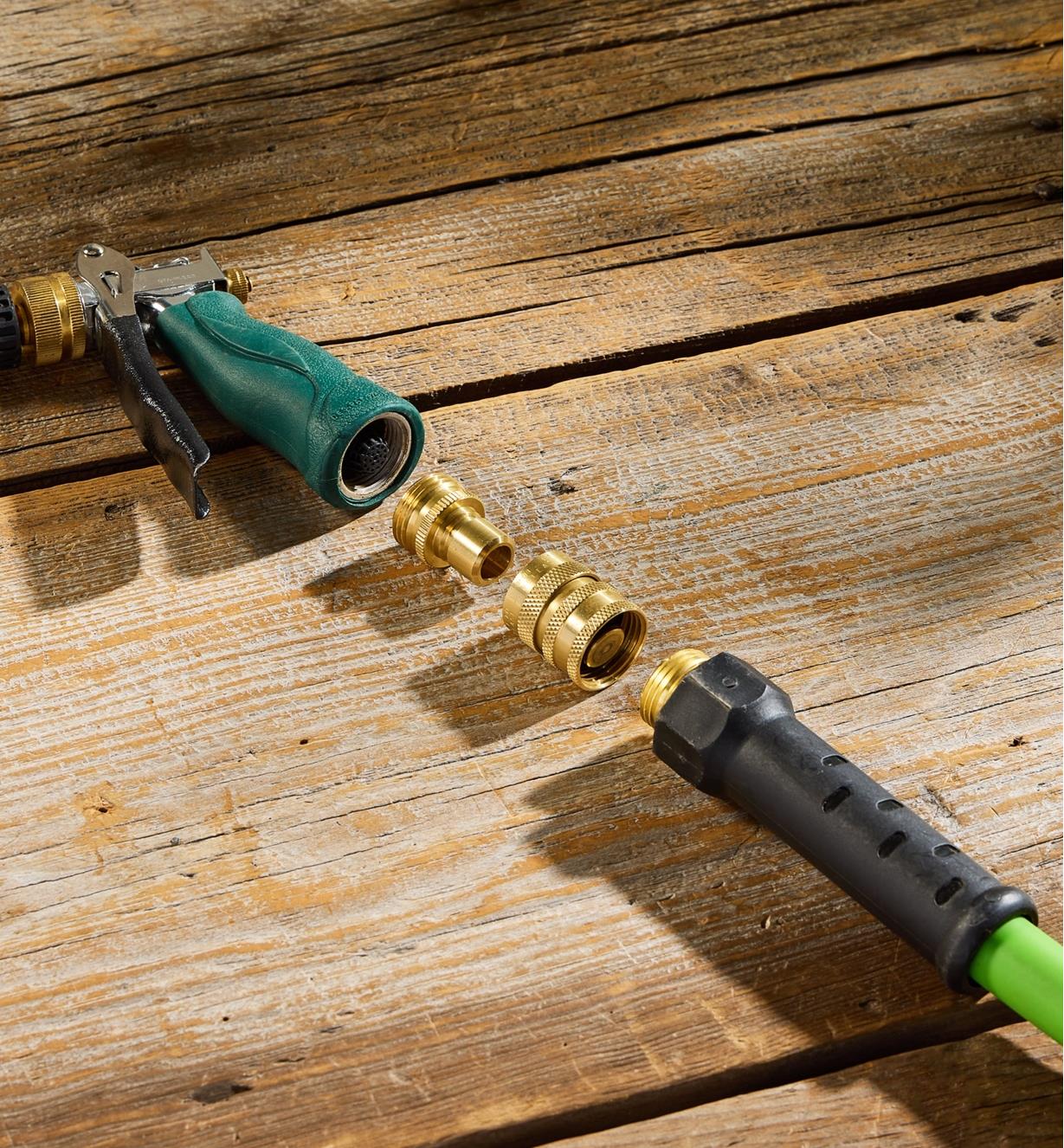 A hose end along with a female and male quick connect and hose nozzle lie flat on a wood surface