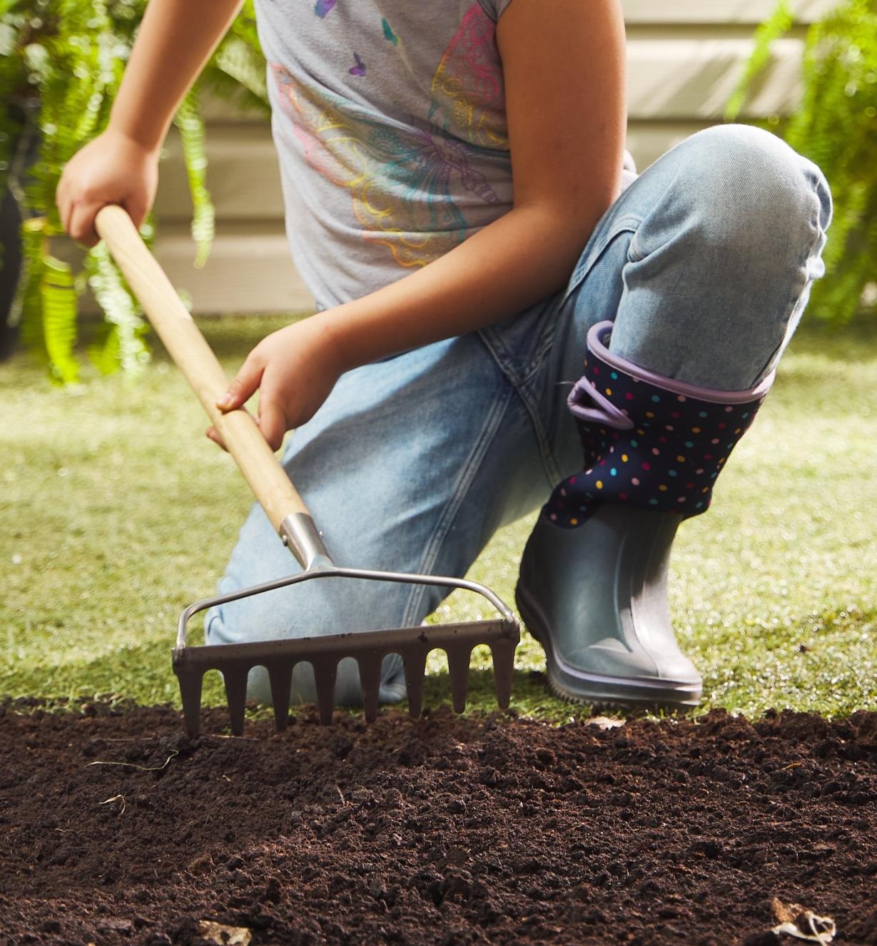 Enfant accroupi raclant le sol à l'aide d'un râteau pour enfant