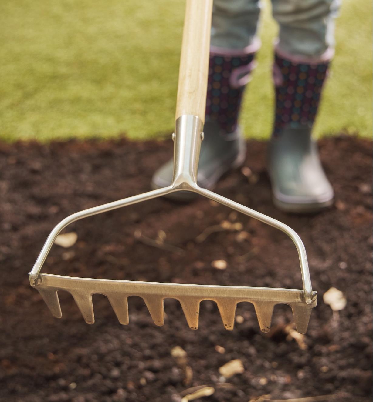 A child uses the children’s rake to move soil outdoors