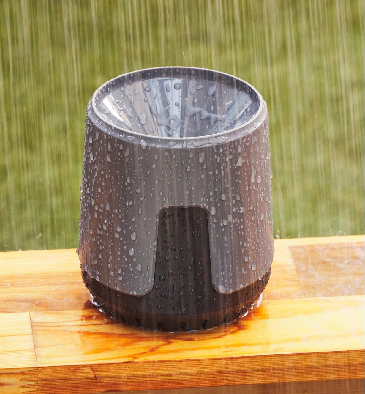 The rain gauge sits on an outdoor wooden surface as it is raining