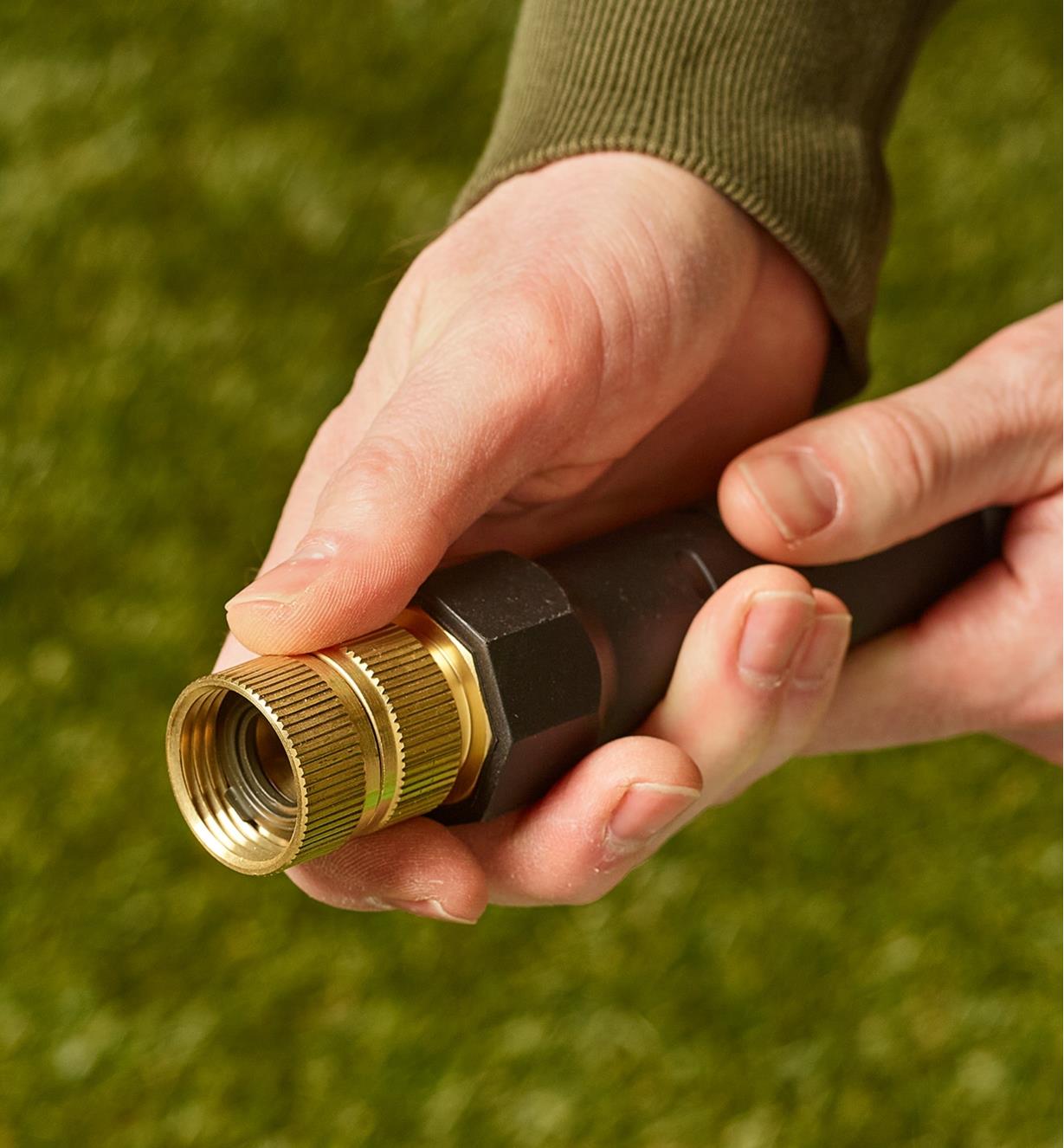 A person holds the end of a hose in both hands with a swivel double female adapter attached