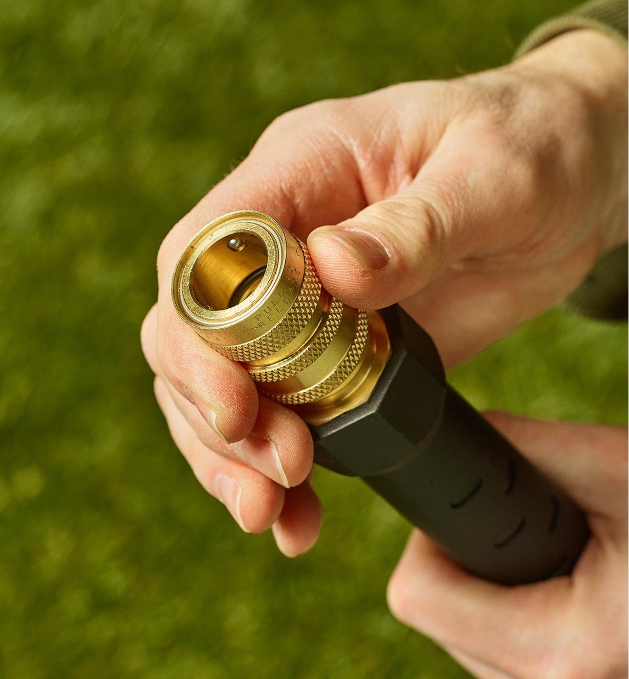 A person grips the brass water stop coupler attached to the end of a hose