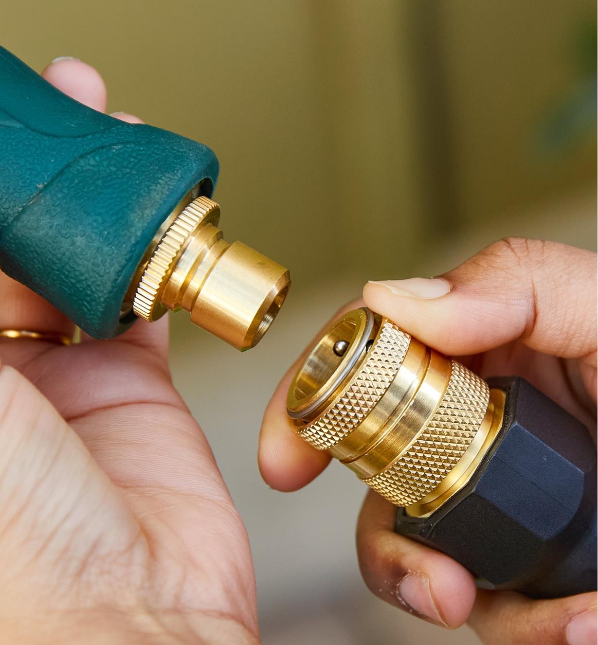 One hand holds a hose nozzle with a male tool adapter while the other holds the end of a hose with a female coupler attached