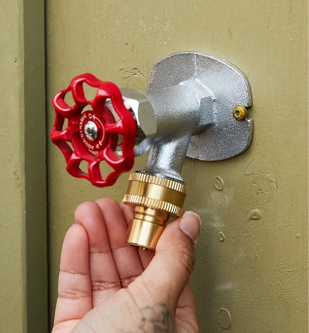 A person grasps a female tap-end adapter that is connected to an outdoor tap