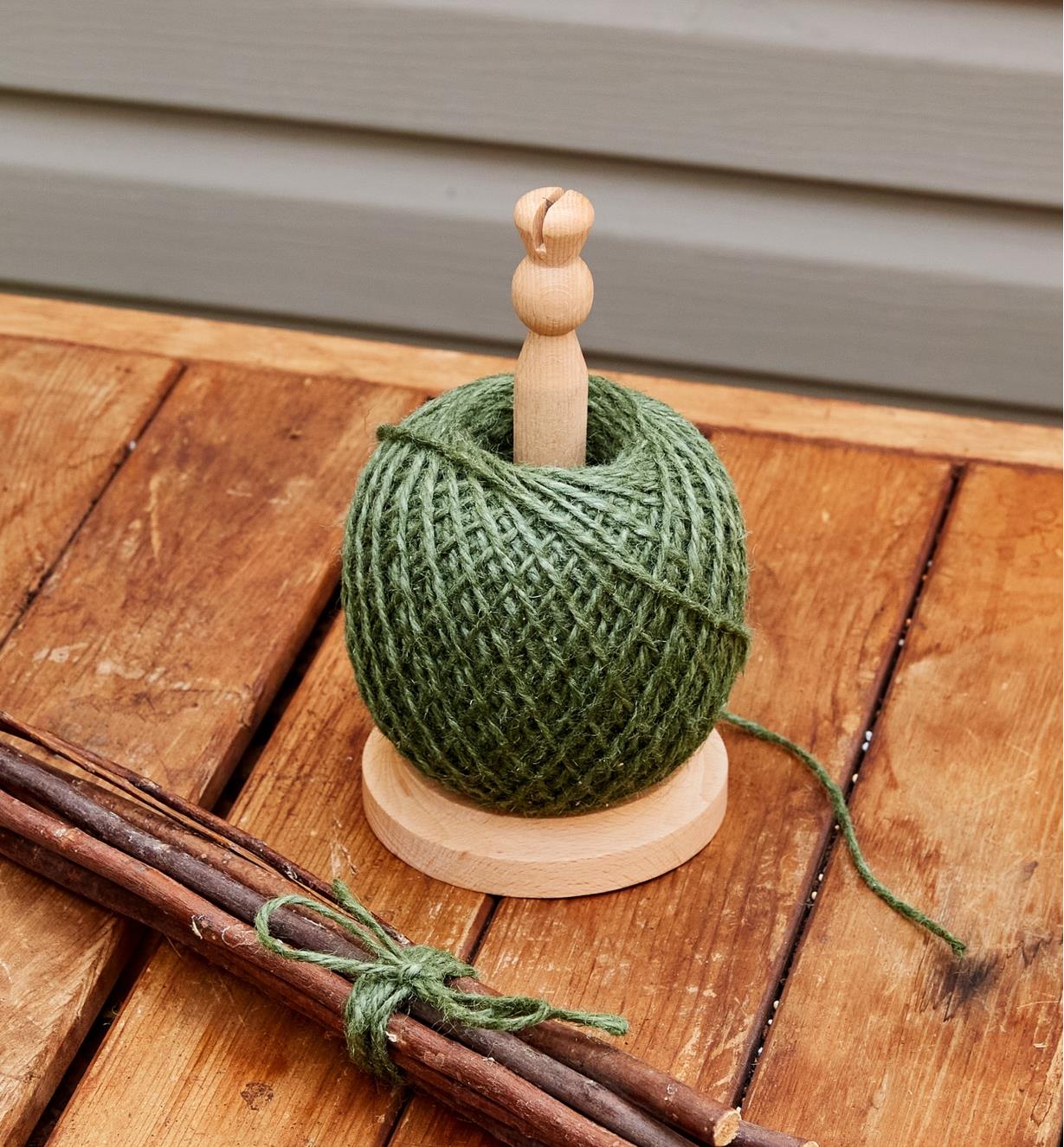 A ball of garden twine on a twine dispenser sits on a wood table next to a bundle of sticks