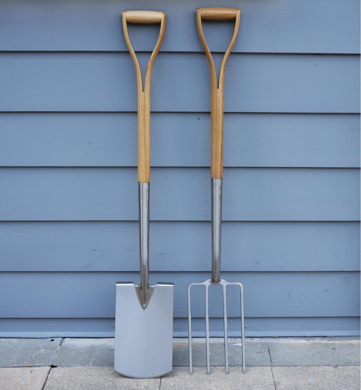 The digging spade and fork stand side by side and are leaning up against an exterior wall